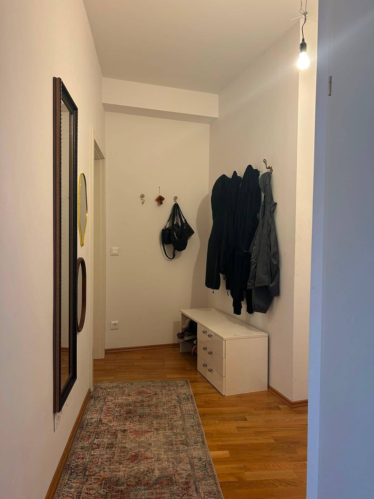 Eingangsbereich mit Garderobe, Schuhbank und einem großen Spiegel auf Holzfußboden.