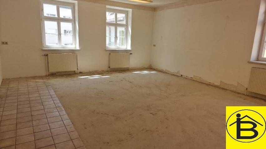 Großer Raum mit Fenstern und Heizkörpern, teilweise mit Fliesenboden und Betonuntergrund.