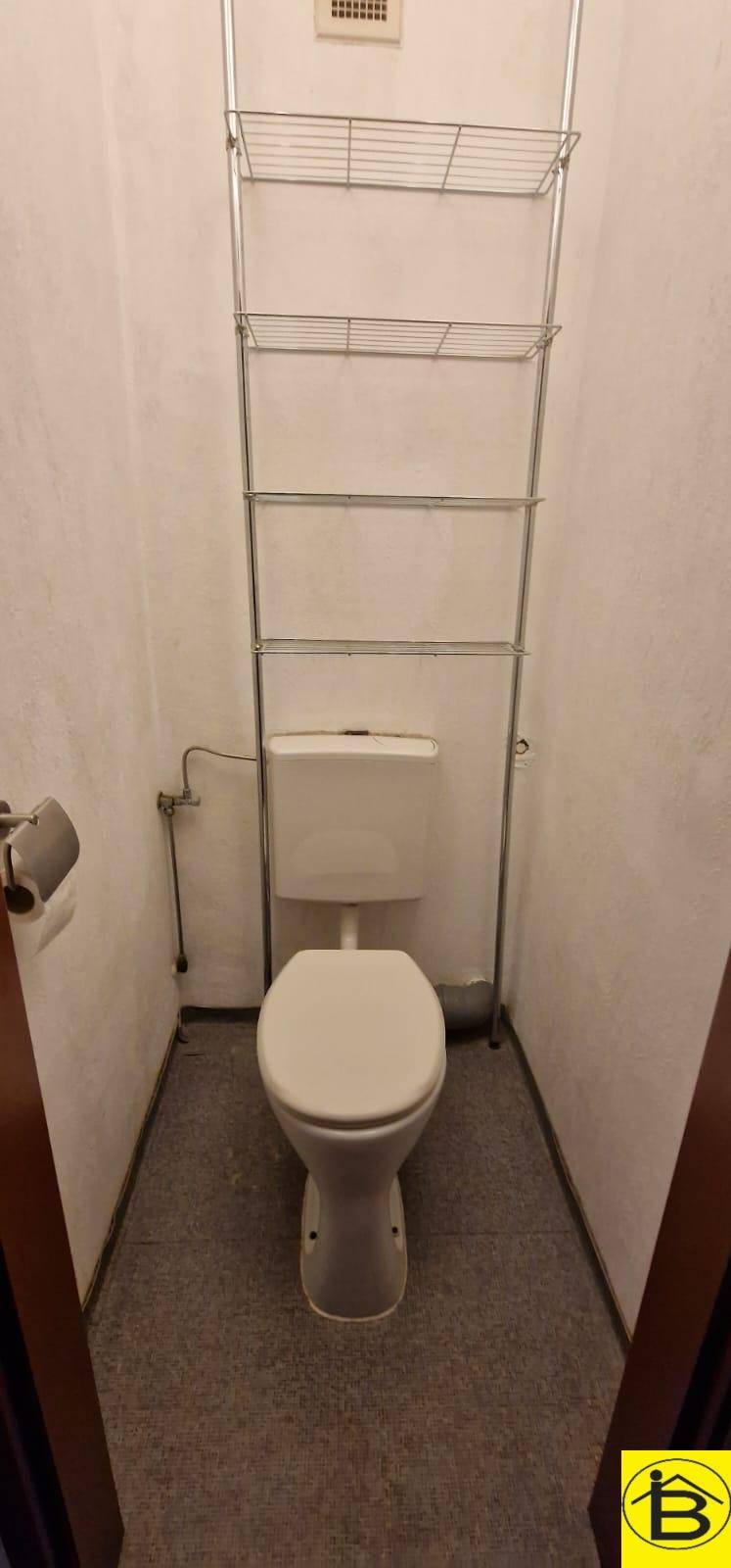 Kleines separates WC mit weißer Toilette und praktischem Regal für Stauraum.