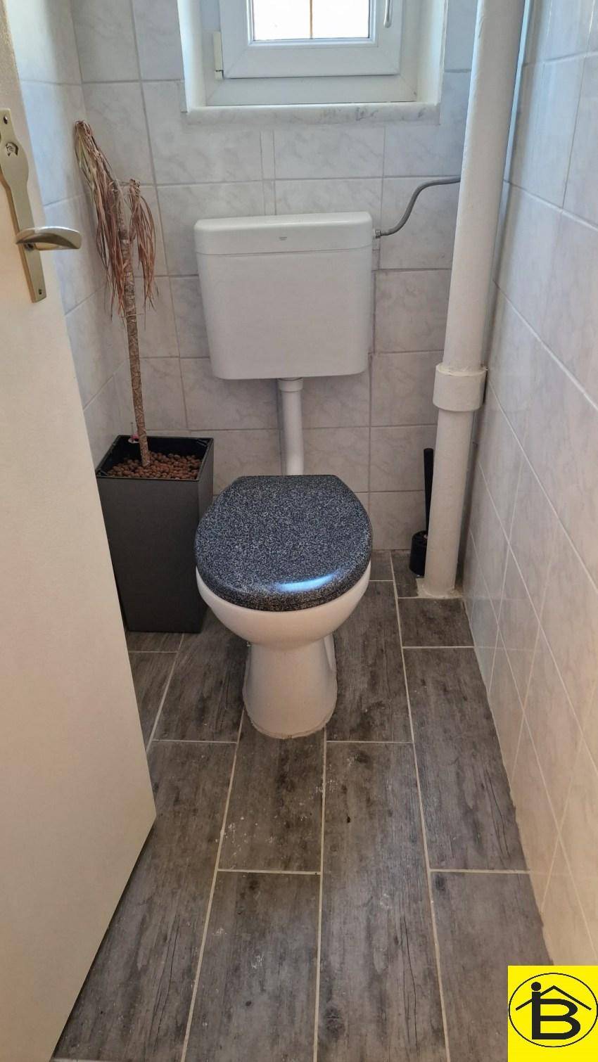 Kleines WC mit Fliesenboden und Fenster, ausgestattet mit einer Standardtoilette und Fliesen.