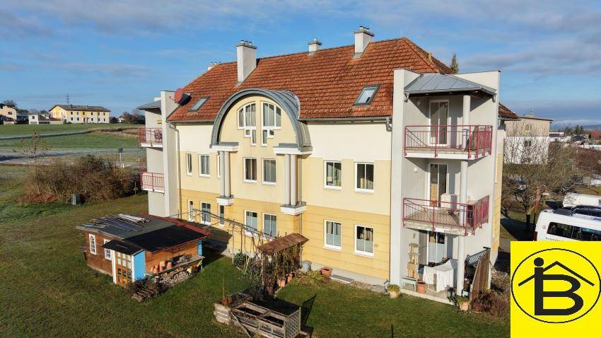 Ansicht des Mehrfamilienhauses mit gelber Fassade, roten Ziegeldächern und mehreren Balkonen.