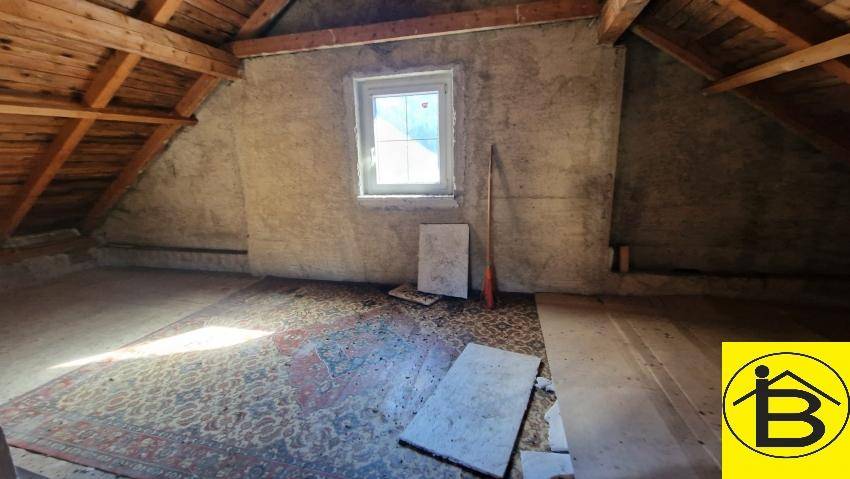 Unausgebauter Dachboden mit sichtbaren Holzbalken und einem Fenster, ideal zum Ausbau.