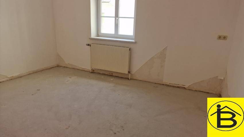Unmöblierter Raum mit einem Fenster und Heizkörper, die Wände zeigen Spuren früherer Nutzung.