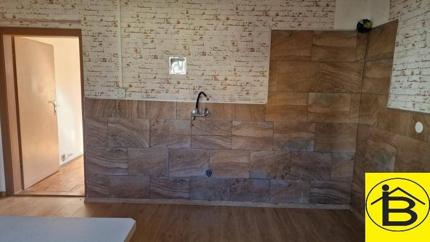 Detailansicht der Küchenwand mit gefliestem Bereich und Wasseranschluss für eine Spüle.