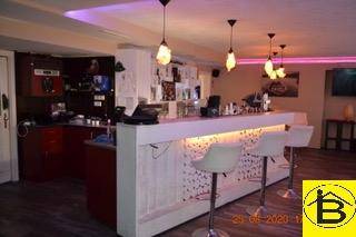 Moderne Bar mit beleuchteter Theke, Barhockern und Deckenleuchten in einem lebhaften Ambiente.