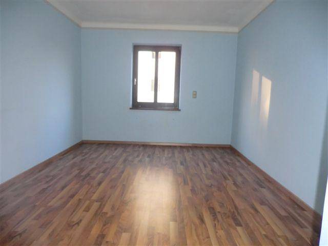 Leeres Zimmer mit blauen Wänden und Laminatboden, ein Fenster sorgt für Tageslicht.