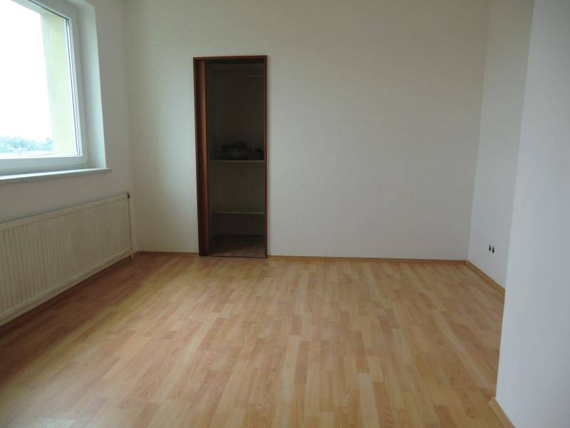 Leeres Zimmer mit Laminatboden, weiß gestrichenen Wänden und einem Fenster, das Tageslicht hereinlässt.