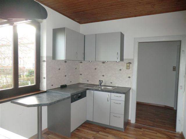 Funktionale Küche mit grauen Einbauschränken, Spüle, Geschirrspüler und kleinem Frühstückstresen am Fenster.
