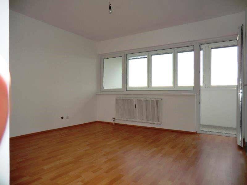Helles Wohnzimmer mit Laminatboden, großen Fenstern und Zugang zu einem Balkon.