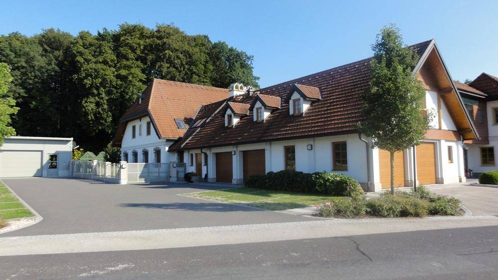 Ansicht des Anwesens mit mehreren Gebäudeteilen, Garagen und einer breiten Zufahrt.