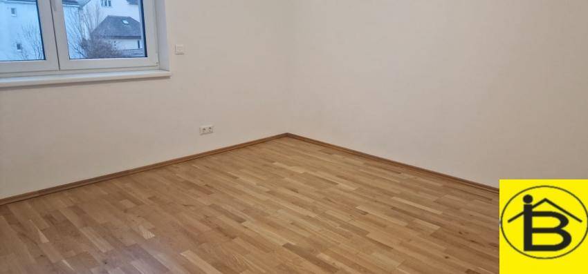 Helles Zimmer mit Holzboden und Fensterblick auf die umliegenden Gebäude und Bäume.