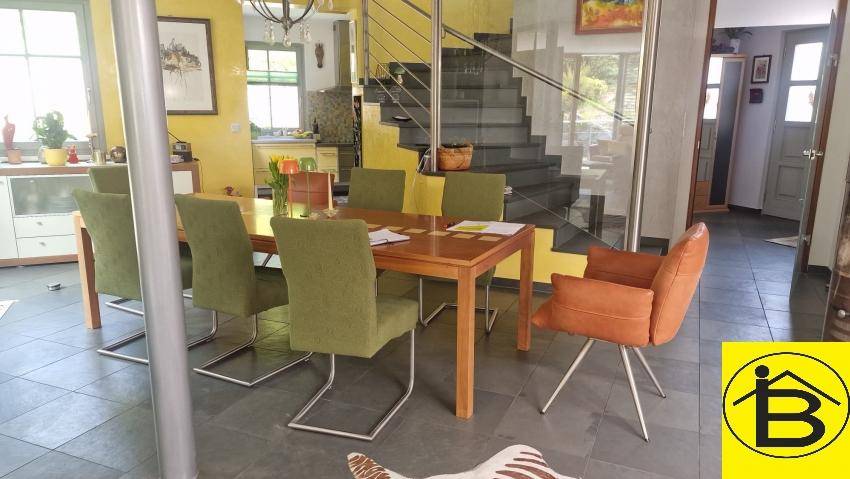 Essbereich mit Holztisch, grünen Stühlen und moderner Treppe mit Glasgeländer.