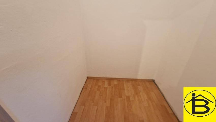 Leerer Raumeck mit Holzboden und hellen Wänden, unmöbliert.