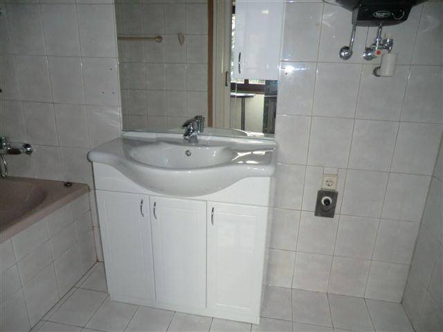 Badezimmer mit Waschtisch, Spiegel und weißen Wandfliesen, die Eckbadewanne ist teilweise sichtbar.