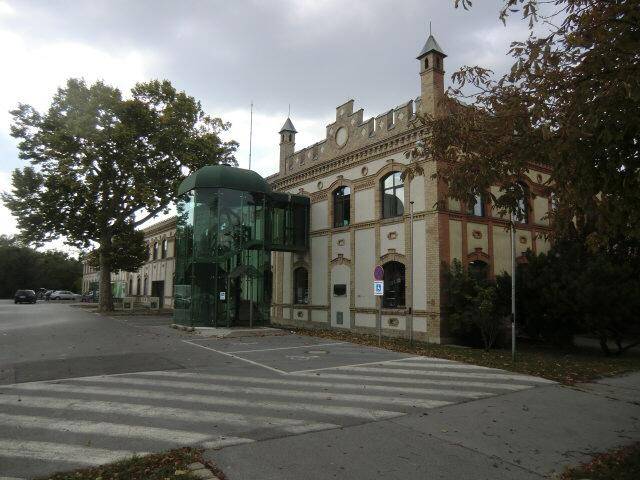 Gesamtansicht des historischen Gebäudes mit modernem Glasanbau und Parkplätzen.