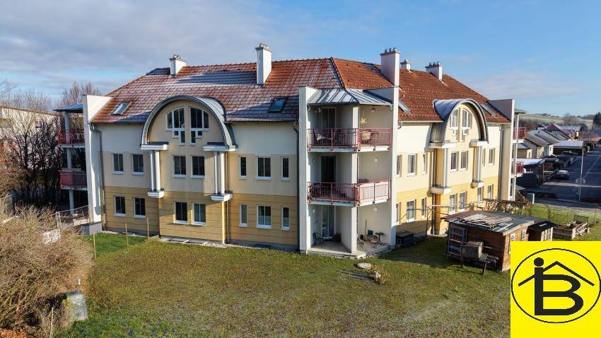 Gesamtansicht des Mehrfamilienhauses mit gelber Fassade, roten Ziegeldächern und gepflegtem Gartenbereich.