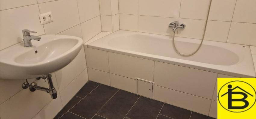Helles Badezimmer mit Badewanne und Waschbecken, ausgestattet mit weißen Fliesen.