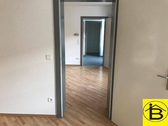 Blick durch einen Türrahmen in einen weiteren Raum mit Holzparkettboden und weiß gestrichenen Wänden.