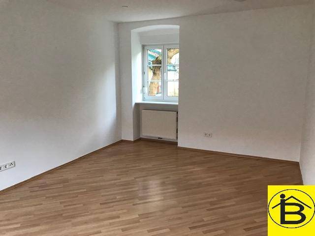Geräumiger, leerer Raum mit Holzparkettboden und einem Fenster mit Blick nach draußen.