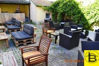 Große Außenterrasse mit verschiedenen Sitzgelegenheiten und Pflastersteinen, umgeben von Grün.