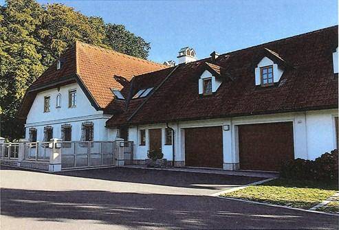 Ansicht der Gebäudefassade mit Garagen, Zufahrt und gepflegter Umgebung unter blauem Himmel.