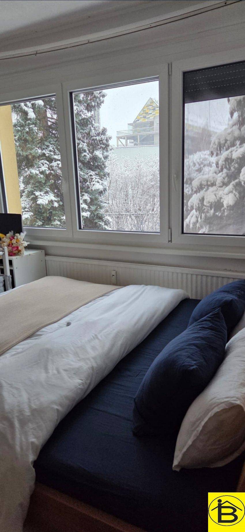 Schlafzimmer mit Bett, großen Fenstern und winterlichem Blick auf verschneite Bäume.