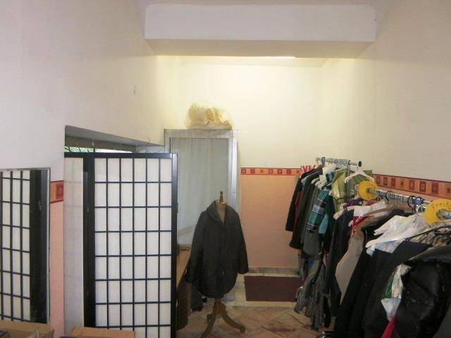 Innenansicht eines Ladenraums mit Kleiderständern, einer Schneiderpuppe und einem Raumteiler, hell gestrichene Wände.