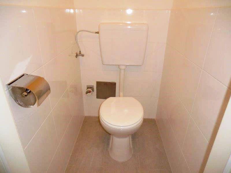 Separates WC mit weißen Fliesen und einer Standardtoilette, funktional und sauber.