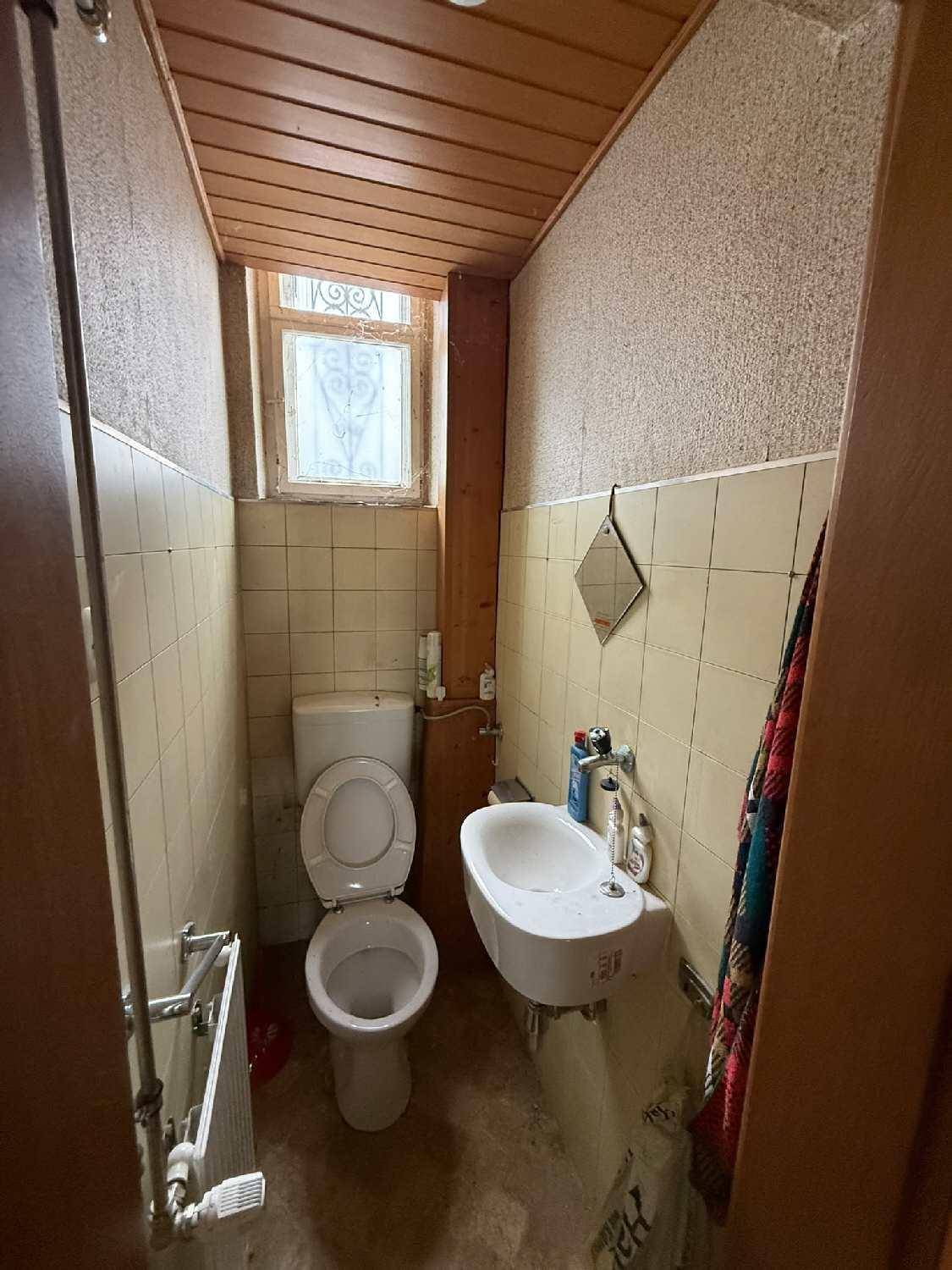 Kleines WC mit Toilette, kleinem Waschbecken, Fenster und gelben Fliesen.