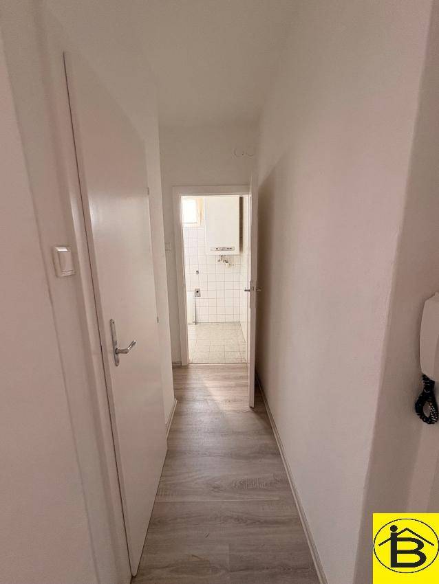 Flur mit Laminatboden, der zu einem Badezimmer mit Fliesen führt, bietet einen klaren Durchgang.