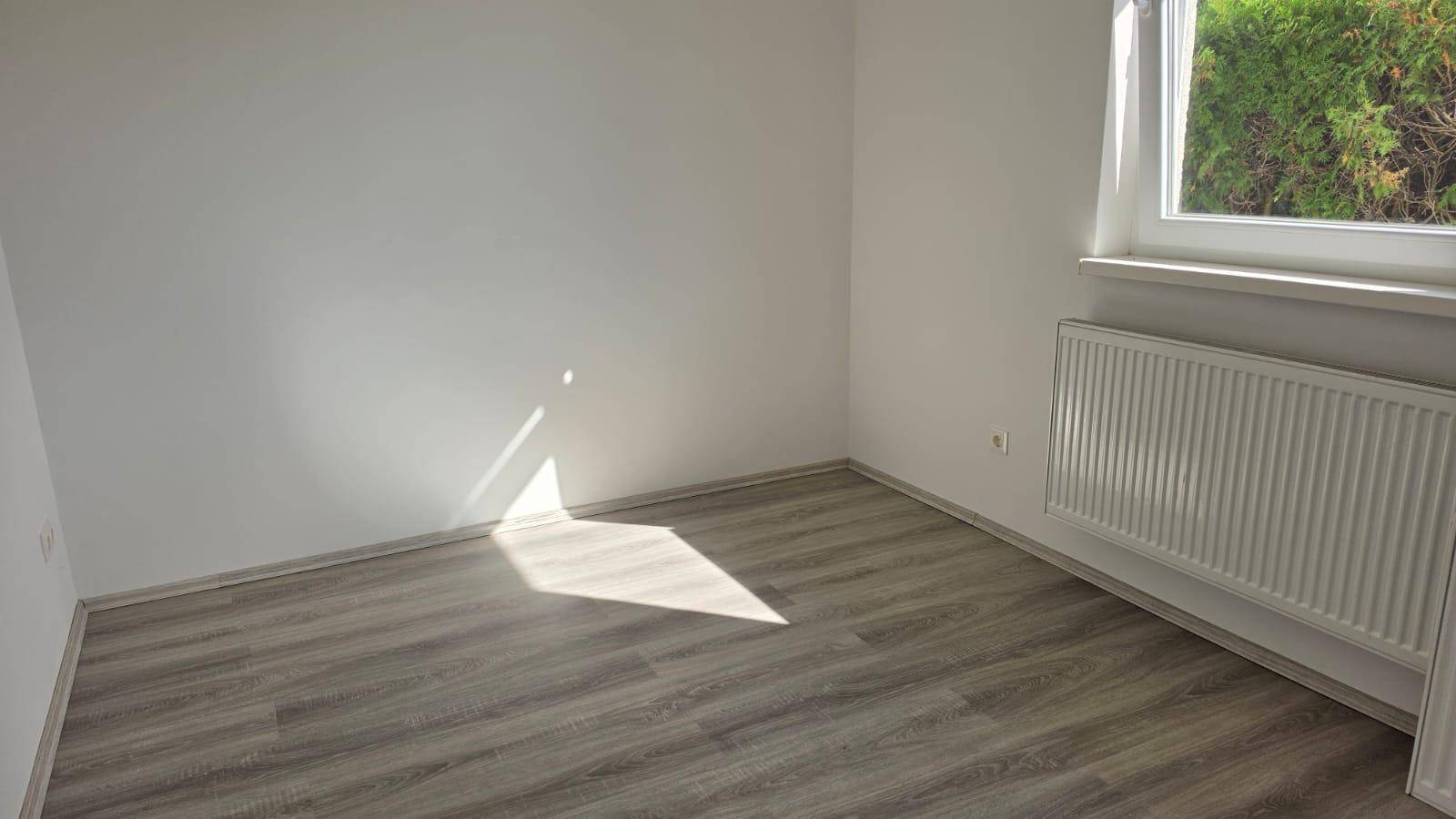 Helles Schlafzimmer mit Laminatboden und Fenster mit Blick auf die grüne Umgebung.