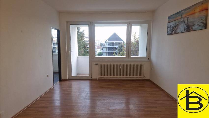 Helles Wohnzimmer mit Laminatboden, großem Fenster und Zugang zum Balkon.