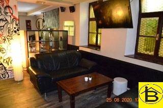 Entspannter Loungebereich mit schwarzem Ledersofa, Couchtisch und dekorativen Fenstern.