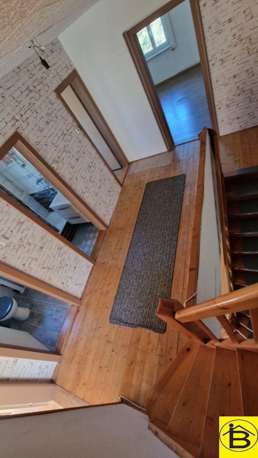 Holztreppe und Flur mit Holzboden und Ziegelstein-Tapete, verbindet verschiedene Stockwerke.
