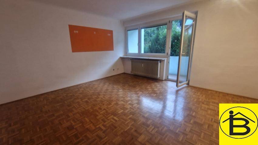 Heller Raum mit Parkettboden und Zugang zu einem Balkon mit Blick ins Grüne.