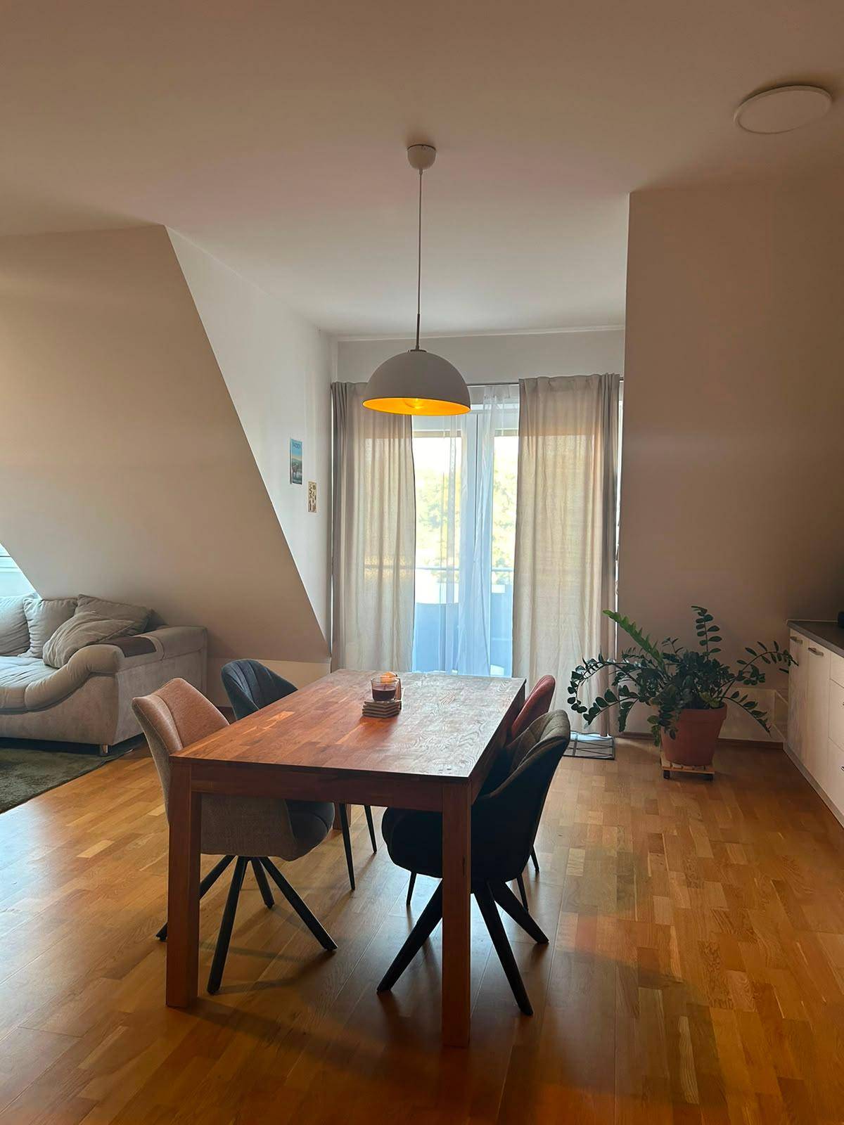 Heller Essbereich mit Holztisch und Zugang zu einem Balkon oder einer Terrasse, ergänzt durch eine Dachschräge.