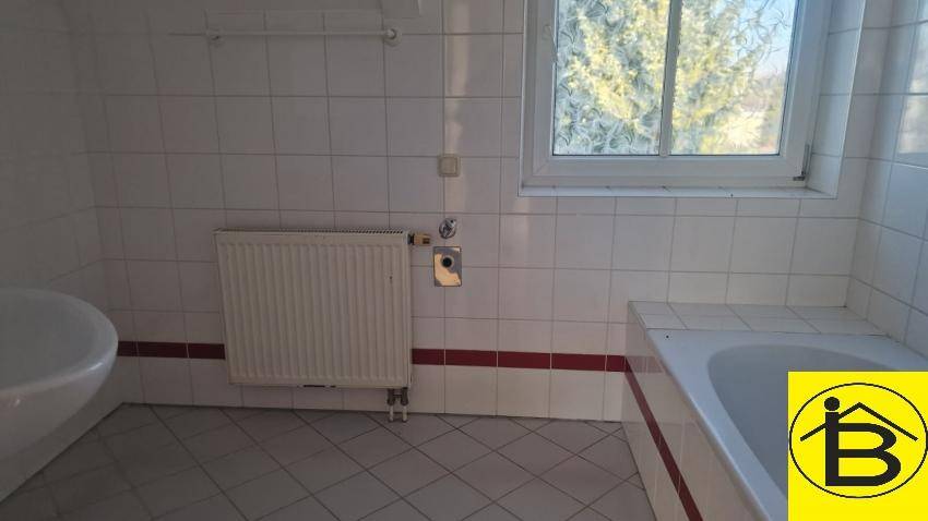 Gefliestes Badezimmer mit Badewanne, Waschbecken und Fenster, in gutem und hellem Zustand.