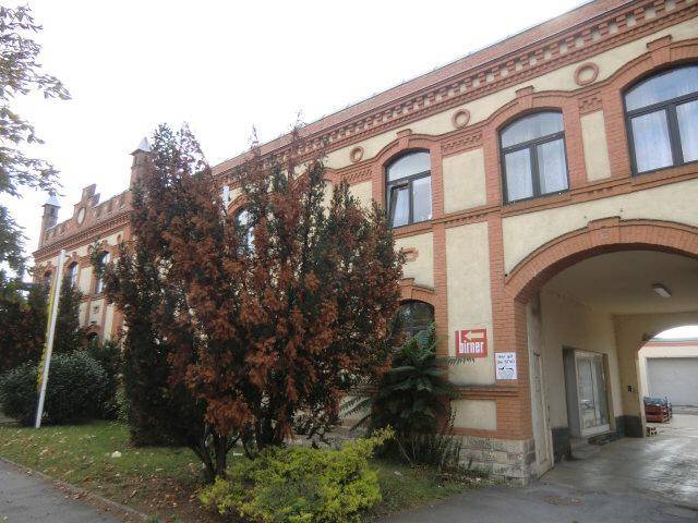 Seitenansicht des historischen Gebäudes mit einem großen Torbogen und Bäumen davor.