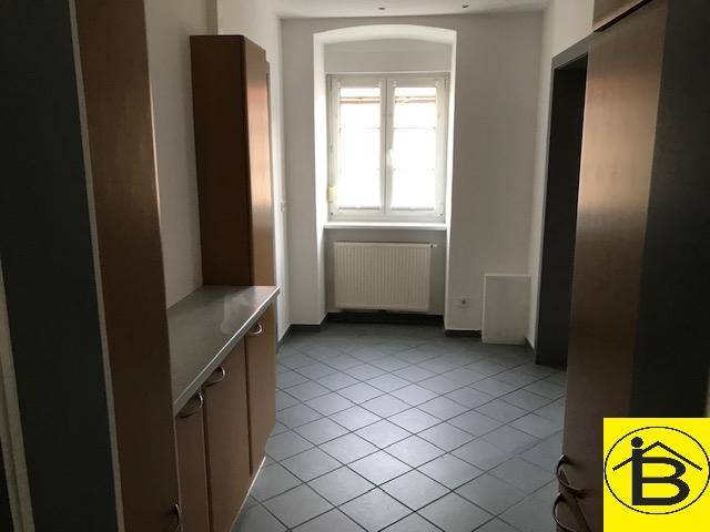 Funktionaler Raum mit braunen Schränken, Fliesenboden und einem Fenster mit Heizkörper.