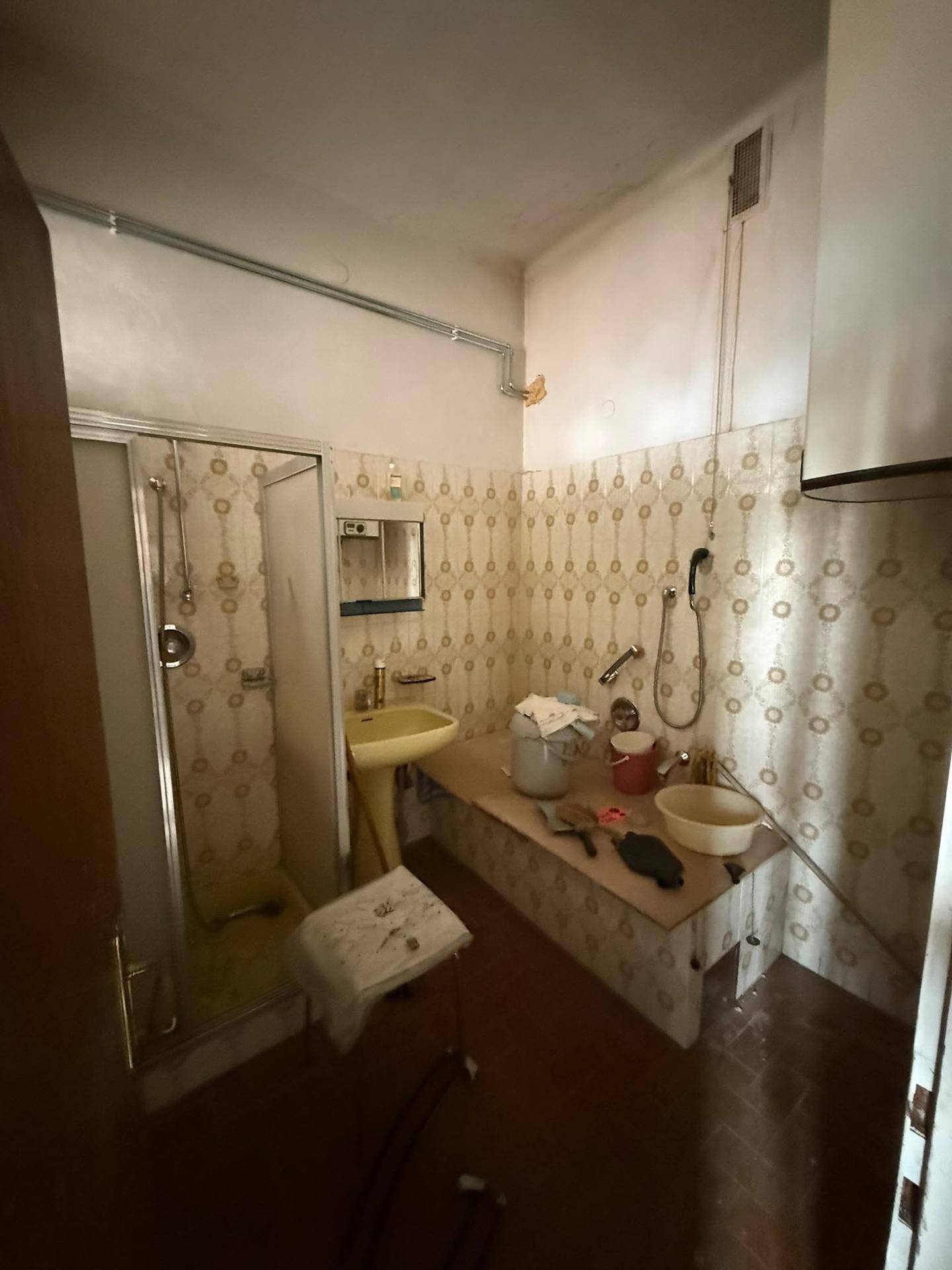 Badezimmer mit gemusterten Fliesen, einem Waschbecken und einer Duschkabine, im älteren Stil.