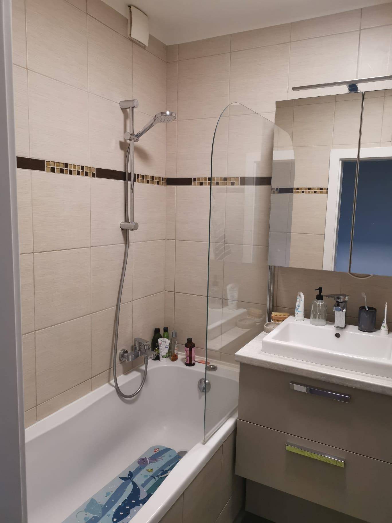 Badezimmer mit Badewanne, Duschvorrichtung, beigen Fliesen und Spiegelschrank.