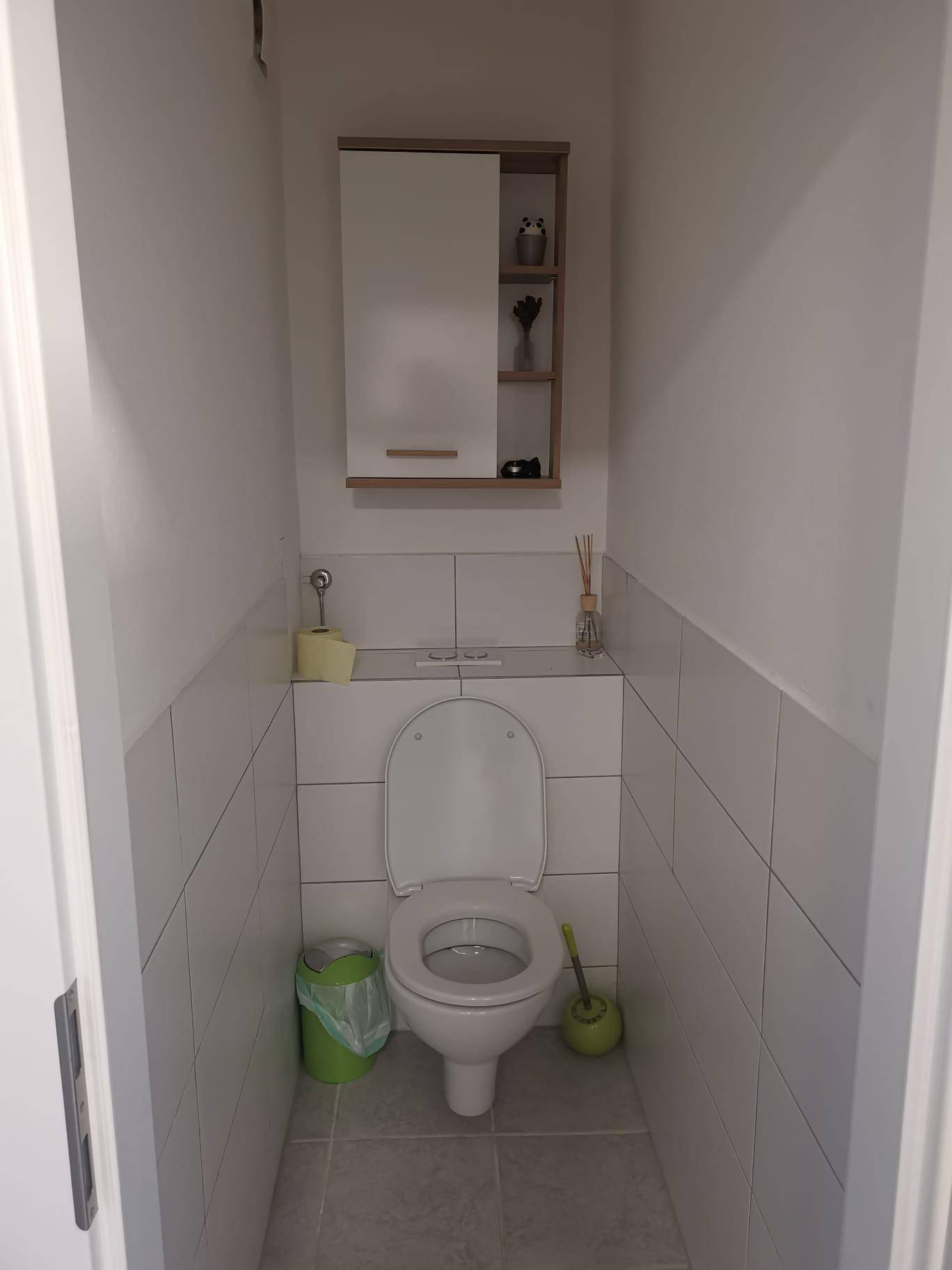 Separates Gäste-WC mit Wand-WC, halbhohen Fliesen und kleinem Wandschrank.