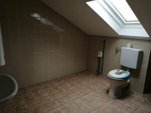 Badezimmer mit Toilette, Dachfenster und beigefarbenen Fliesen.