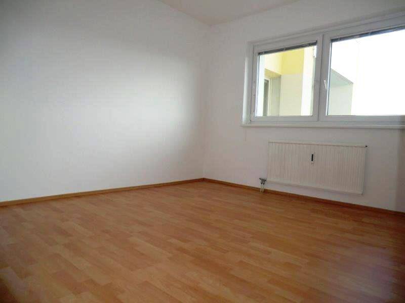Helles Zimmer mit Laminatboden, weißen Wänden und einem Heizkörper unter dem Fenster.