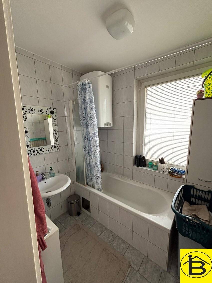 Gefliestes Badezimmer mit Badewanne, Waschbecken und Fenster, funktional und hell.