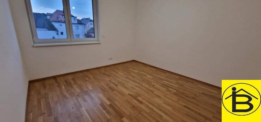 Helles Zimmer mit Holzboden und Fensterblick auf die umliegenden Gebäude und Bäume.
