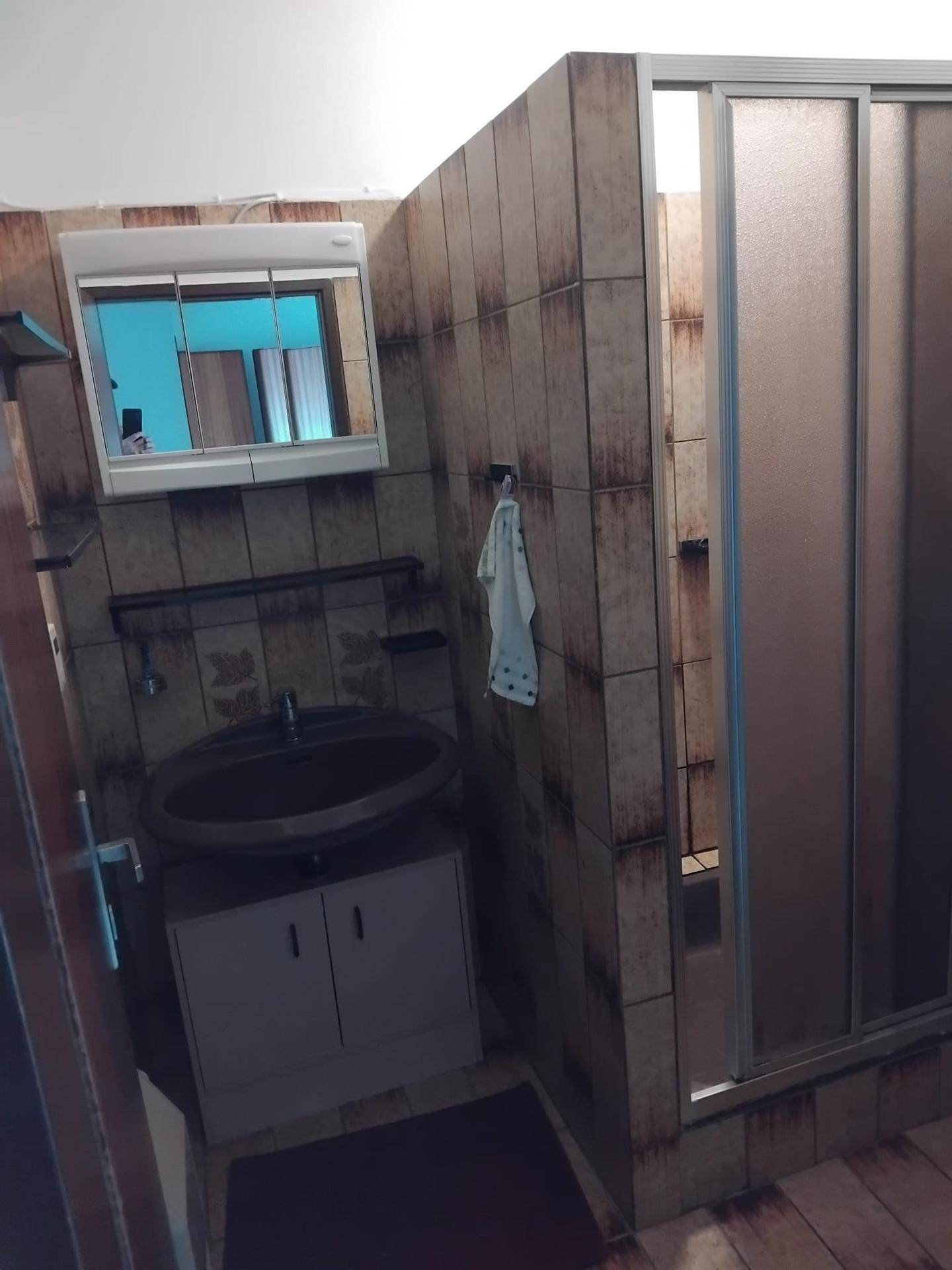 Badezimmer mit Waschbecken, Spiegelschrank und Duschkabine, gefliest in Brauntönen.