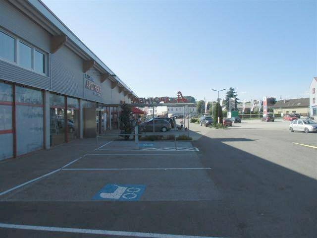 Parkplatz vor einer Apotheke und weiteren Geschäften, mit klarem Himmel und Sonnenschein.