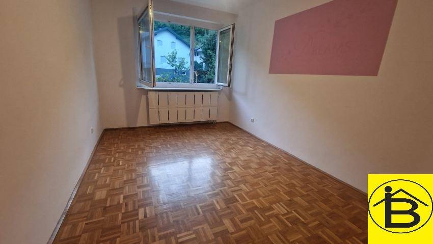 Geräumiger, unmöblierter Raum mit Parkettboden und Fensterblick ins Grüne.