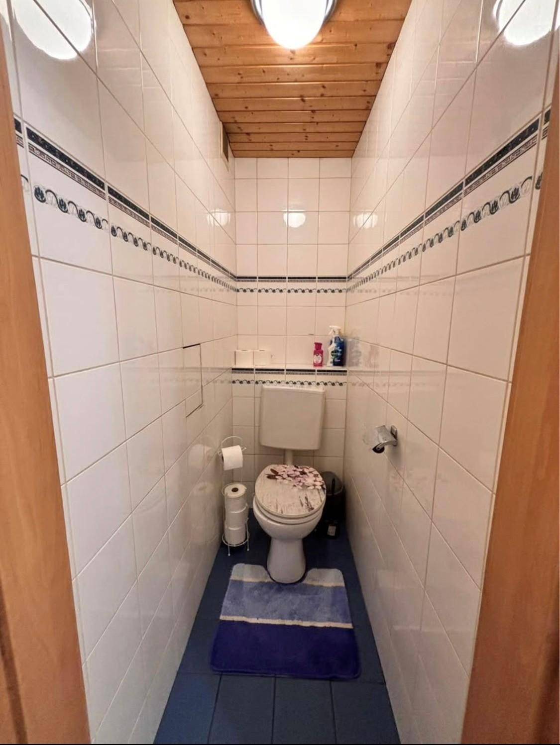 Kleines separates WC mit weißen Wandfliesen, Holzdecke und einem wandmontierten WC.